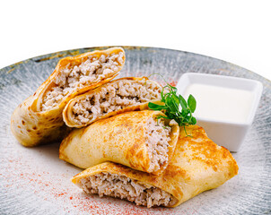 Pancakes with meat filling lying on gray plate with sour cream