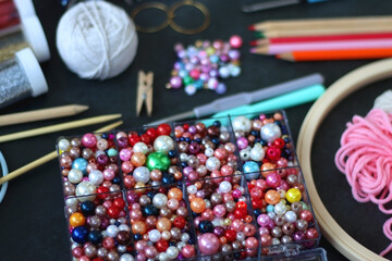 Colorful beads, coloring pencils, glitter, needles, string, hoop, tape and scissors on dark...