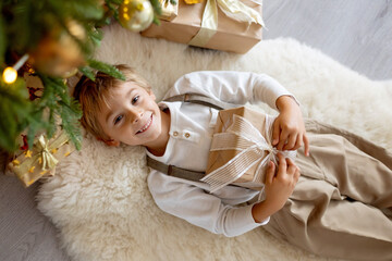 Sweet blond child, cute boy, playing with christmas toys on Christmas, beautifully decorated home for Christmas, cosy place