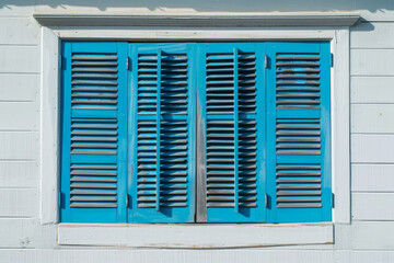 Fototapeta premium Bright blue wooden shutters on a white wooden house in daylight
