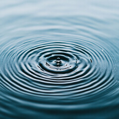 A drop of water is falling into a large body of water. The water is calm and still, with ripples forming around the drop. Concept of tranquility and peacefulness