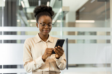Confident professional woman using smartphone in modern office environment. Wearing glasses, she engages with digital technology for communication and productivity in professional setting.