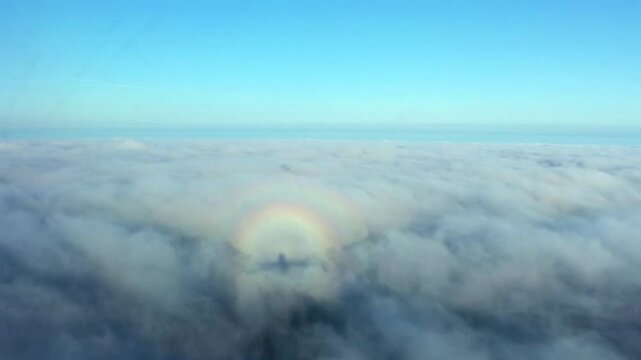 Circular halo or Glory round rainbow on clouds seen from cockpit during descent with airplane shadow