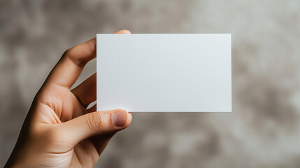 Fototapeta premium White Business Card Held by Hand Against Textured Grey Background