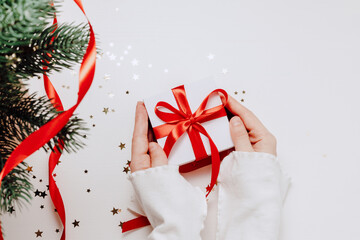 Festive christmas gift box in woman hands with confetti and Christmas tree, top view.
