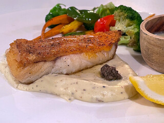 Delicious grilled fish fillet with creamy sauce, fresh vegetables, and a lemon slice, perfect for a gourmet meal.