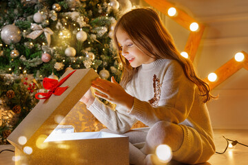 Happy girl opening x-mas presents. Children with gift boxes and christmas star. Decorated living room with traditional fire place.