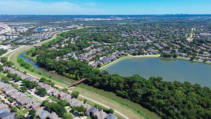 Coppell Texas suburban park lush green trees, lake, creek near upscale residential neighborhood row of two-story houses with pools, interexchange stack and downtown Dallas in background, aerial