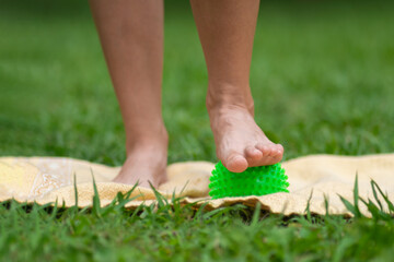 Close-up of a woman's foot with a prickly massage ball on a mat in the park. Myofascial relaxation, massage of the fascia of the foot with a ball, fitness, self-care, health, smart fitness.