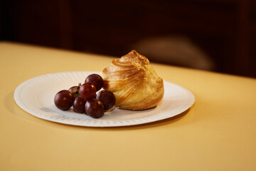 A dessert of profiteroles and grapes presented on a white plate, close-up for promotional purposes.