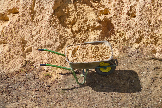 A wheelbarrow filled with sand against the backdrop of a sand pile, manual removal of sand, unloading of construction sand