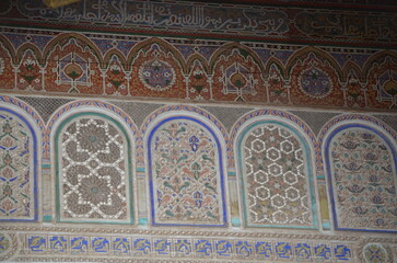 Ornate Moroccan wall with intricate geometric and floral patterns, featuring traditional Islamic calligraphy at the top. The detailed craftsmanship showcases rich cultural heritage in Marrakesh.
