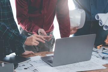 Architects and engineers point to blueprints of architectural drawings inside a building to discuss construction plans, with hard hats and architectural documents scattered around. Close-up.