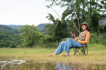 Fototapeta premium Fisherman man fishing with a spinning fishing rod in hand, close-up on the bank of a river or lake. With the light scene during the sunset against the natural forest in the background Hobby,fisherman.