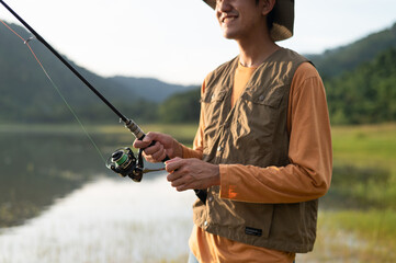 Fisherman man fishing with a spinning fishing rod in hand, close-up on the bank of a river or lake. With the light scene during the sunset against the natural forest in the background Hobby,fisherman.