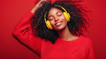 Young African American woman in red, enjoying music with yellow headphones, joyful and expressive on a red background.