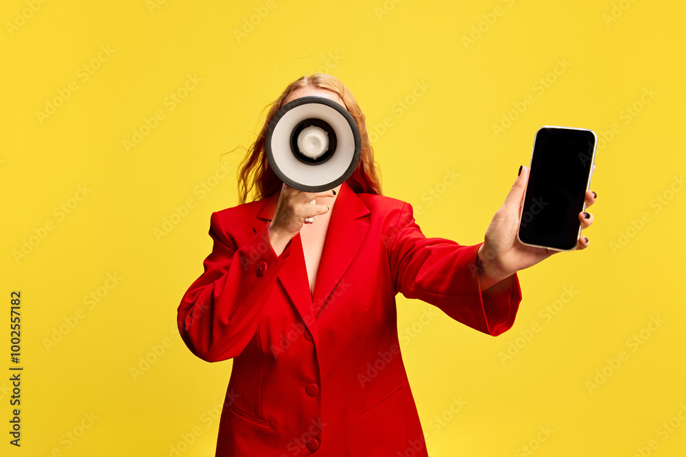 Wall mural woman in red jacket, with megaphone and mobile phone in hands against yellow studio background. new 