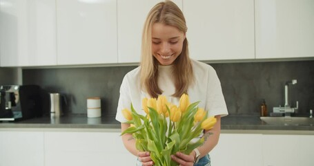 A young woman admiring a bouquet of yellow tulips in a bright, modern kitchen, creating a peaceful and uplifting atmosphere with natural lighting and minimalist decor