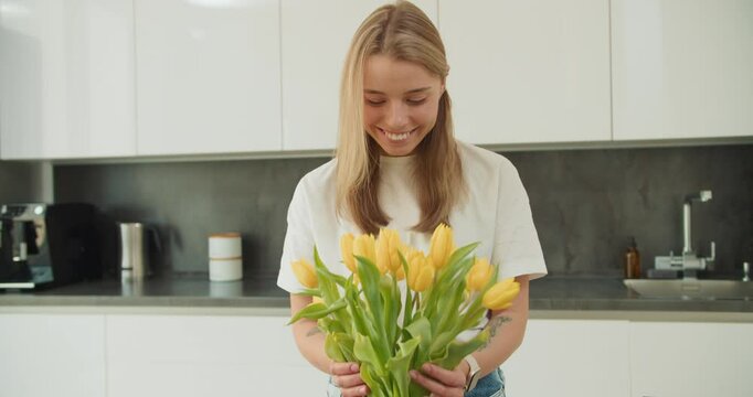 A young woman admiring a bouquet of yellow tulips in a bright, modern kitchen, creating a peaceful and uplifting atmosphere with natural lighting and minimalist decor
