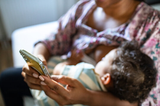 Mother breastfeeding while using smartphone at home