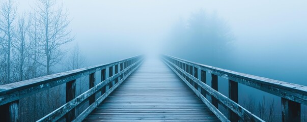 Fototapeta premium A tranquil wooden bridge disappearing into a blue fog, evoking a serene and mysterious atmosphere in nature.