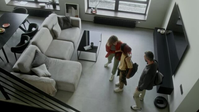 Wide top shot of affluent Caucasian husband and wife bringing African American orphan home from orphanage after adoption, welcoming into spacious new house, showing around and hugging with excitement