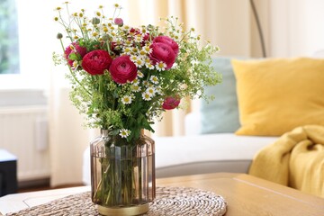 Beautiful ranunculus flowers and chamomiles in vase on table indoors