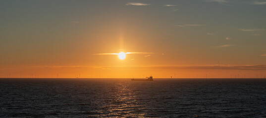Obraz premium Panorama at sunset over the North Sea with a silhouette of a ship and a wind farm on the horizon.