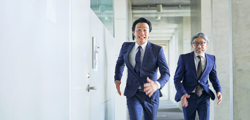 ビルの通路を走る二人のビジネスパーソン