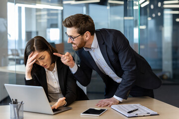 Businesswoman looking stressed as angry boss confronts her about work at office desk. Scene...