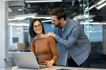 Man and woman inside office at workplace, colleagues flirting and courting each other, businessman massaging colleague's shoulders.