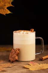 Autumn Raf coffee with espresso, maple syrup and whipped cream foam decorated ground cinnamon in a ribbed glass cup. Yellow maple leaves and cookie on background. Autumn still life. Space for text