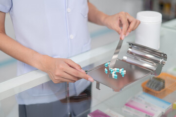 Asian professional female pharmacist standing with arms crossed looking at camera charming smile pointing hand to pill bottle health care products in pharmacies Close-up and wide-angle shots