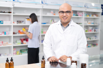Asian professional male pharmacist using digital tablet computer checking drug list Pharmacist checking stock in pharmacy for health medicine in pharmacy with female pharmacist in the background