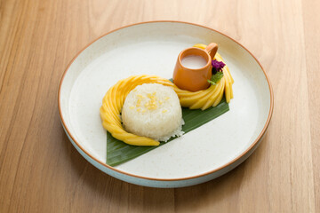 A classic Thai delight, mango sticky rice, steals the spotlight with its vibrant presentation: ripe mango, fragrant sticky rice, mung beans, and coconut milk unite on a banana leaf canvas.