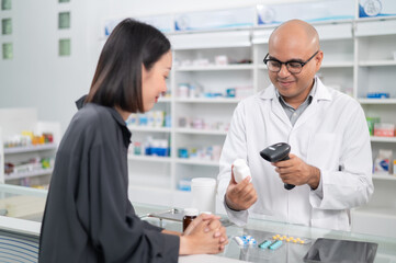 Obraz premium Asian professional male pharmacist using a tablet to dispense prescription medicines to female customers. The doctor advises and explains to the client how to use the medication.