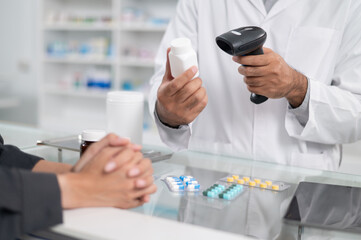 Asian professional male pharmacist using a tablet to dispense prescription medicines to female customers. The doctor advises and explains to the client how to use the medication.