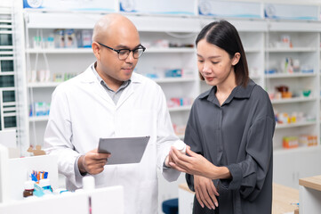Asian professional male pharmacist using a tablet to dispense prescription medicines to female customers. The doctor advises and explains to the client how to use the medication.