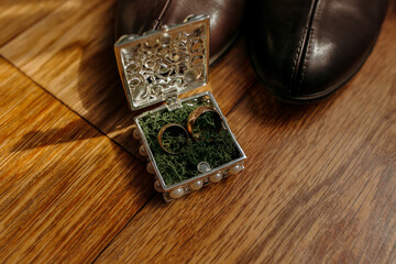 A small box with two gold rings inside sits on a wooden floor