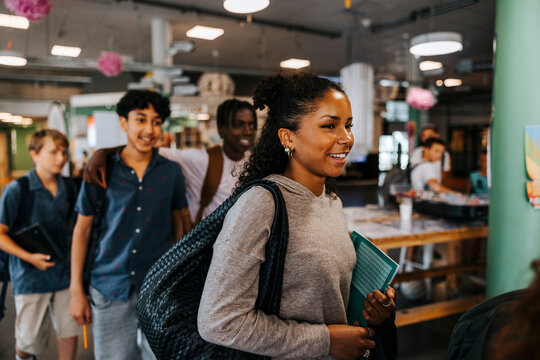 Smiling teenage girl with bag walking in cafeteria at junior high school