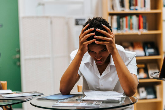 Worried teenage boy sitting with head in hand while studying at library of school