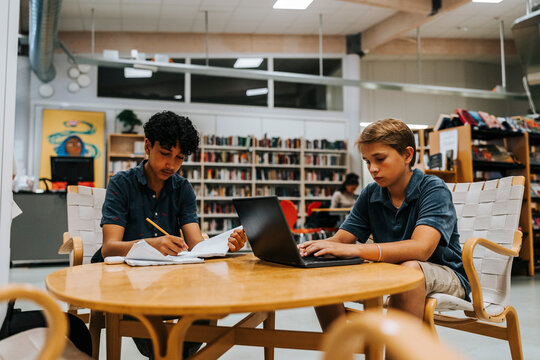 Focused male students studying while sitting near table in library at junior high school