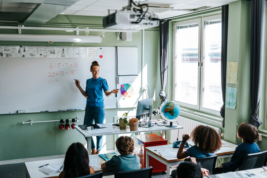 High angle view of female professor teaching mathematics to group of multiracial students in classroom at school