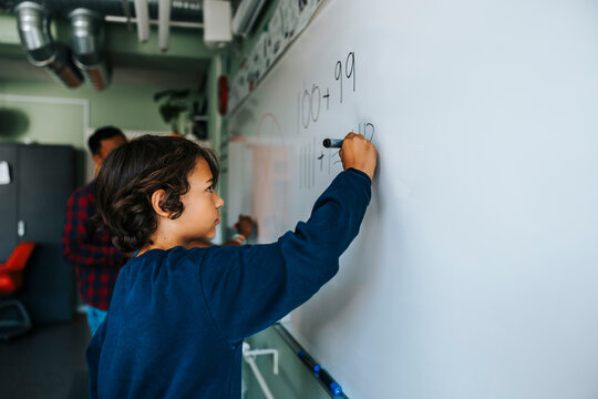 Side view of boy solving mathematics equation on whiteboard in class at school