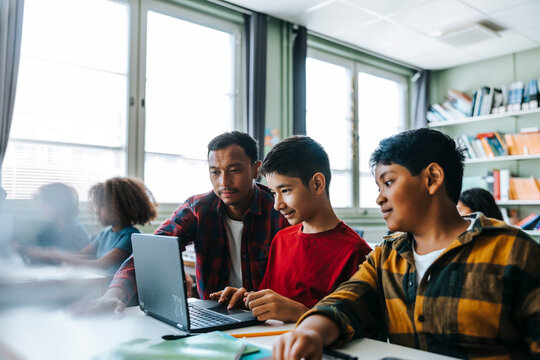 Male teacher assisting student studying on laptop in classroom at elementary school - Powered by Adobe