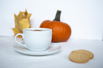 white mug with coffee against the background of pumpkin and yellow leaves