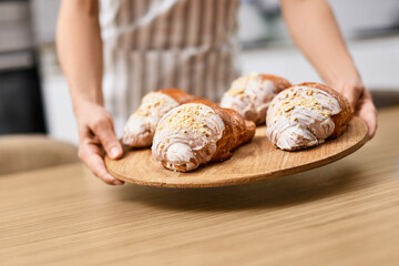 female baker holding wooden tray with freshly baked crispy golden croissants