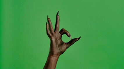 Creepy halloween devil monster hand in black paint with nails shows ok good finger sign, isolated on chroma key green screen background, workspace mockup.