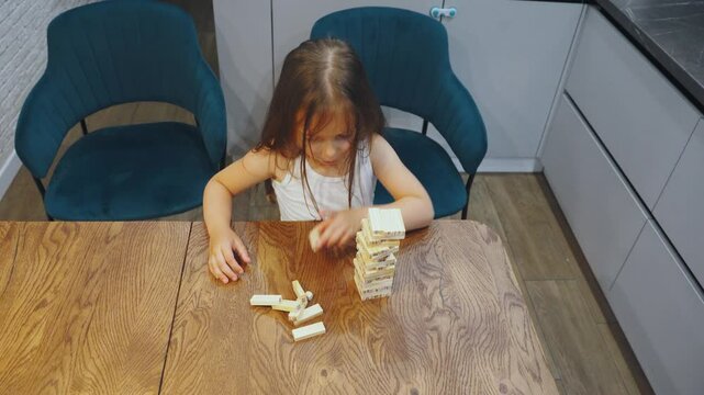 In a cheerful kitchen, a young girl joyfully builds a wooden block tower, showcasing her imagination. This playful activity nurtures her cognitive development, intelligence, and critical thinking