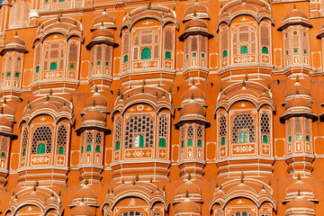  a close-up view of the intricate facade of the Hawa Mahal in Jaipur, India. The architecture features beautifully designed jharokhas (windows) with fine latticework, domed canopies, and vibrant earth